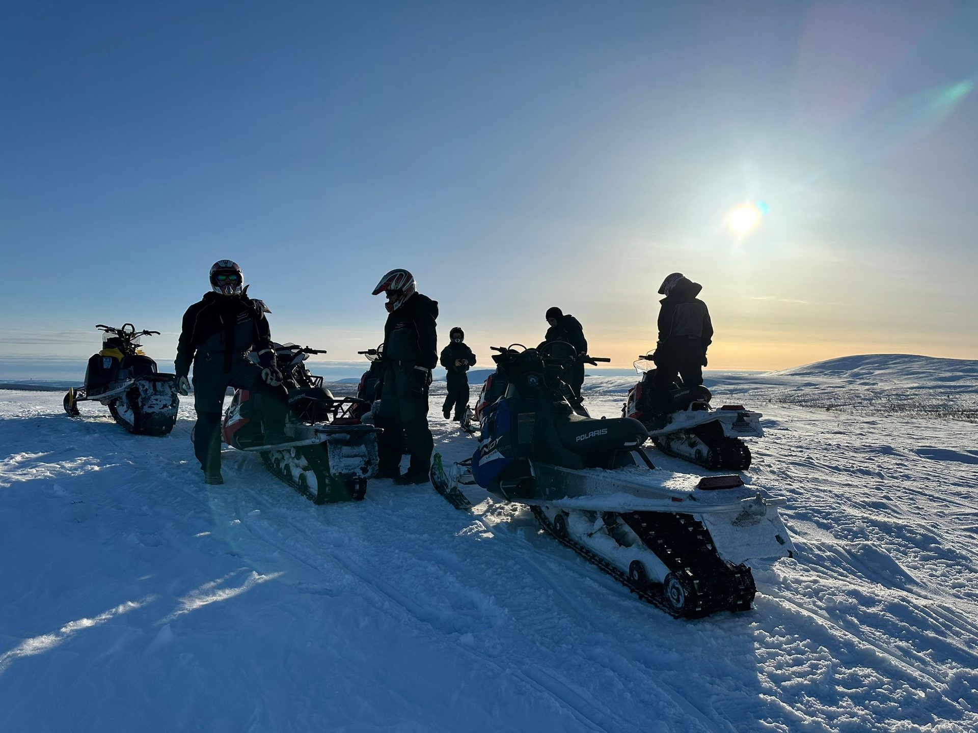 Gruppe mit Snowmobilen im Sonnenuntergang